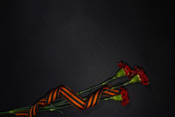 Three Red carnations tied with St. George ribbon on black background. Symbolized a victory day in...