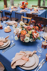 festive tables with tablecloths made of textiles are decorated with flower arrangements, on the tables are candles, plates with napkins, glasses, cutlery, a wedding in the forest, banquet, holiday