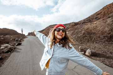 Lifestyle portrait of a carefree stylish woman enjoying a trip on a rocky coast, having fun while walking on the desert road. Happy travel and freedom concept
