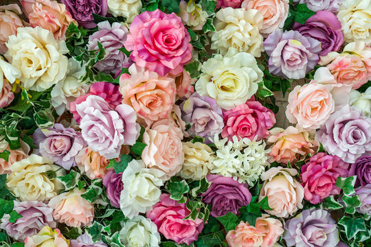 Closeup flatlay top view of many colorful artificial synthetic flowers of pastel red, pink, purple, white and orange colors.