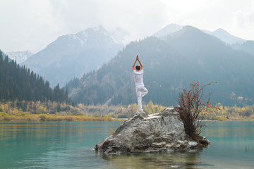 A zen man in white practices yoga in nature. Pose Vrikshasana or tree pose