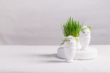 Festive composition Easter eggs in cups and green plant sprouts on a white table. Light background Happy Easter concept. Horizontal frame copy space.