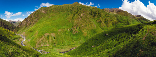 Panoramic view of large and beautiful green valley with big mountains, river and blue sky
