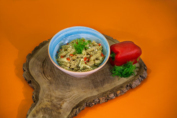 a bowl of fusilli pasta with pepper and dill on orange background.