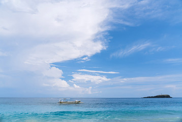 Fototapeta na wymiar Landscape with a turquoise sea and a white fishing boat on the waves. Beaches of Bali. Rest in a heavenly place. Clear water and blue sky