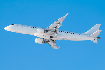 Fototapeta na wymiar Modern white passenger jet plane flies in the air on a clear sunny day against a clear blue sky