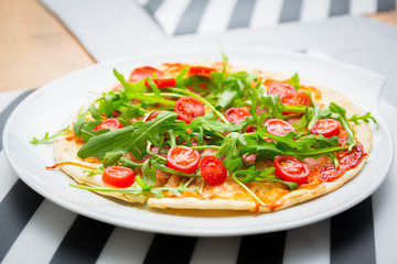 Italian pizza with rocket salad, cherry tomatoes, ham and cheese