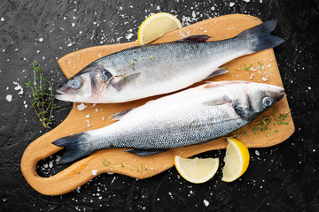 Fresh raw sea bass and ingredients for cooking on black slate table. 