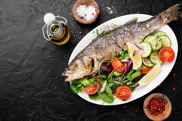 White plate of baked sea bass with fresh green salad.