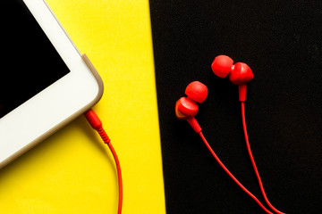 Red earphones in mp3 player on smartphone on black and yellow background