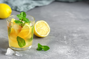 Cold refreshing tea with lemon, mint and ice in a glass on a gray concrete background. Summer drink. Selective focus.