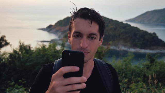 Man Tourist with Backpack Using Smartphone. Traveler on top of a mountain on the background of a tropical island in the sea. Travel concept