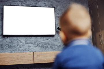 Rear view of focused blond little boy sitting on the floor in living room and watching cartoons on television.