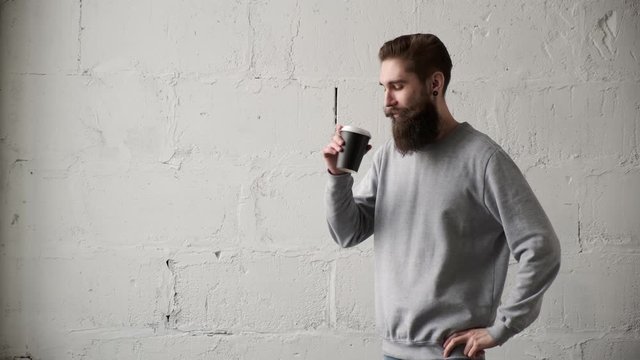 Young bearded man drink coffee looking out window. happy programmer during break