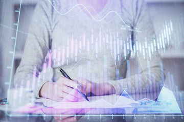 Hand taking notes in notepad. Forex chart holograms in front. Concept of research. Double exposure