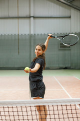 A girl with a tennis racket on a tennis court with artificial lighting looks at the camera