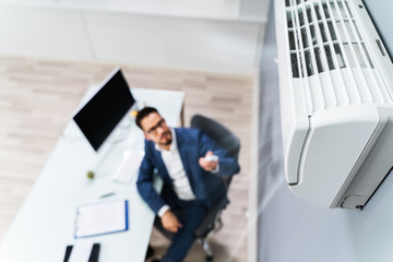 Businessman Using Remote Control In Front Of Air Conditioner
