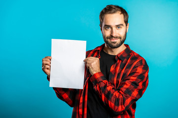 Handsome man holding vertical white a4 paper poster. Copy space. Smiling hipster guy in red plaid...