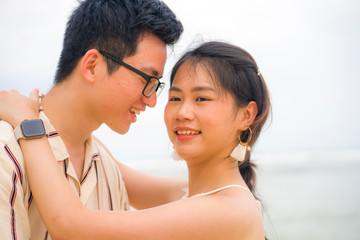 sweet and romantic lifestyle portrait of young happy Asian Korean couple in love enjoying holiday on beautiful beach walking together by the sea playful and affectionate