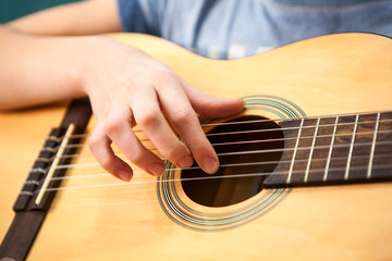 Female hand plucks the strings of a yellow acoustic guitar, close up view
