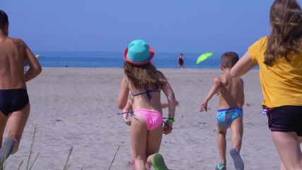 Five children in bright clothes run on the sand towards the sea on a clear sunny day