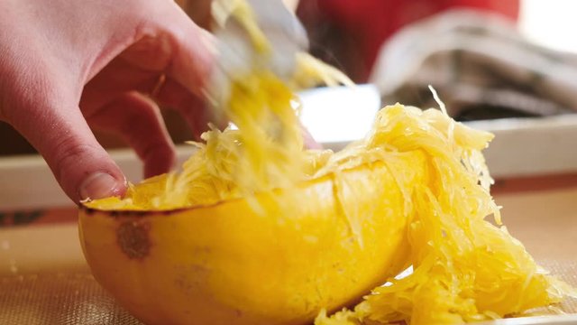 Woman pulling apart spaghetti squash with a fork. The orange strands of the fall vegetable are a delicious pasta alternative for gluten free cooking, paleo diets and plant based cooking.