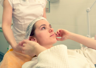 Obraz na płótnie Canvas Young woman patient wearing hair cap at beauty clinic cosmetology service lying on medical bed relaxed while doctor prepares to do the procedure