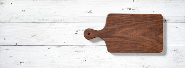 Handmade walnut wood cutting board on white wooden board desktop.
