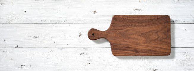 Handmade walnut wood cutting board on white wooden board desktop.