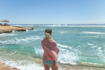 White woman standing alone on sunny beach looking at beautiful windy stormy sea water.