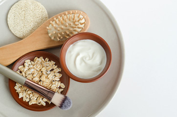 Fresh greek yogurt, oatmeal, cosmetic brush and wooden hairbrush. Natural beauty treatment and zero waste concept. Top view, copy space.