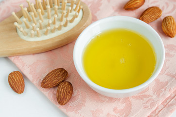 Small glass bowl with almond oil and wooden hair brush for natural hair care. 