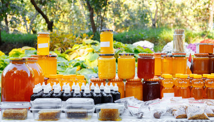 Jars and honey sticks with natural honey on shelf in fair. Sale of natural honey in market outdoor.