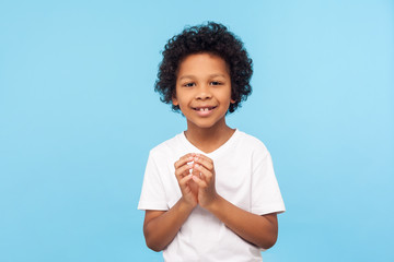 Portrait of funny devious little boy in T-shirt thinking over cunful idea and smiling at camera,...