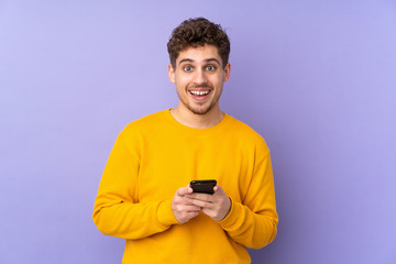 Caucasian man isolated on purple background surprised and sending a message