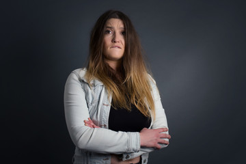 Isolated portrait of stylish young European woman bitting her mouth and looking worried and scared crossing arms, worry and doubt.