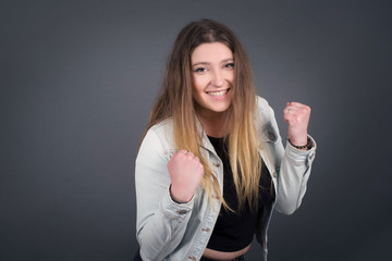 Fototapeta premium Caucasian brunette woman rejoicing her success and victory clenching her fists with joy. Lucky woman with hair bun being happy to achieve her aim and goals. Positive emotions, feelings.