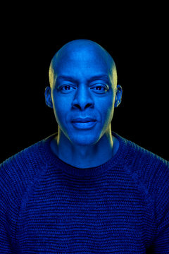 Studio photo of a black man looking at the camera with blue light. Isolated on black background. Vertical