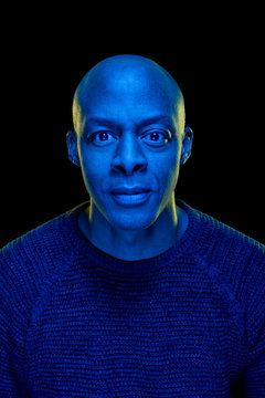 Blue light studio photo of a black man looking at the camera with amazement expression. Isolated on black background. Vertical