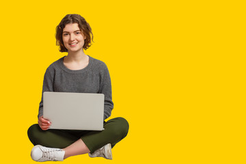 Naklejka premium Pretty Indian asian young girl using laptop computer isolated over yellow background