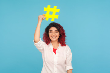 Popular blogs. Portrait of positive woman with fancy red hair holding hashtag symbol on head and...