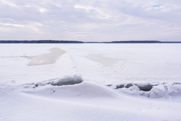 Landscape of a frozen lake in winter. The surface of the water in the lake is covered with snow and ice.