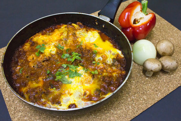 Poached Eggs in Tomato Sauce in pan on cork table mat with raw ingredients. It's called Shakshuka eggs in Mediterranean culture.