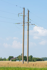 High-voltage power lines in wheat field meadow and blue sky background. High voltage electric transmission towers.