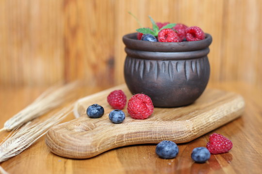 aspberries and blueberries in a brown mug on a light wooden background