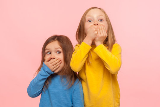 Portrait Of Two Little Frightened Girls Covering Mouth With Hands And Looking With Scared Eyes, Children Afraid To Speak, Taboo Topic, Intimidation. Indoor Studio Shot Isolated On Pink Background