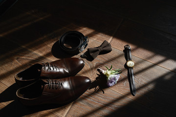 Close up of brown male shoes, bowtie, belt, watches and boutonniere on wood floor background, copy space. Modern man accessories. Wedding details