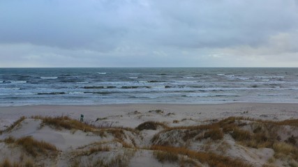 Seascape of large waves and dunes and beach at overcast day