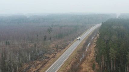 Aerial view over the highway with traffic in the fog, forest landscape.