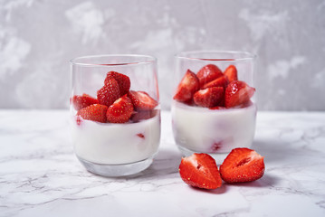 Two glasses of healthy yogurt with fresh sliced strawberry on white table background, copy space. Healthy breakfast, food concept